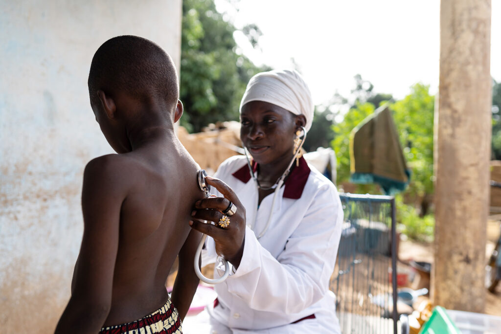 A black female doctor using a stethoscope to listen to the lungs of a young black boy